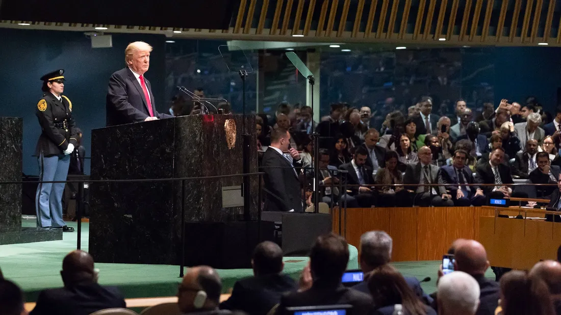 Donald Trump stands at the green marble podium of the UN General Assembly hall, with delegates seated in front of him.