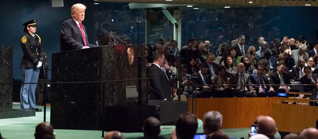 Donald Trump stands at the green marble podium of the UN General Assembly hall, with delegates seated in front of him.