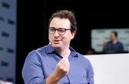 Dario Amodei in a blue shirt and glasses, gesturing as he speaks on stage.