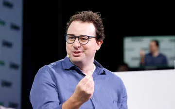 Dario Amodei in a blue shirt and glasses, gesturing as he speaks on stage.