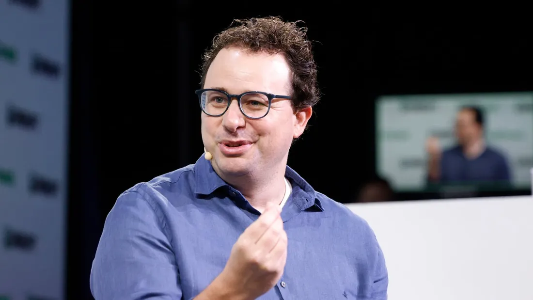 Dario Amodei in a blue shirt and glasses, gesturing as he speaks on stage.
