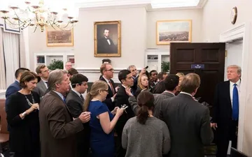 Donald Trump stands in a White House office doorway facing a group of reporters.