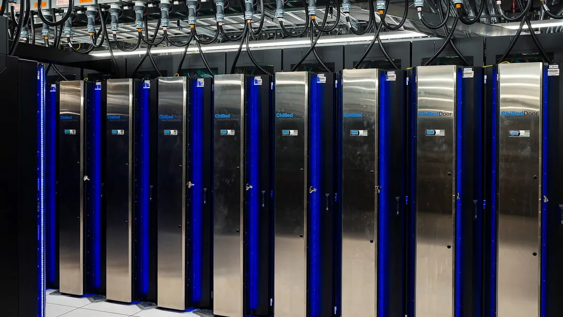 Rows of tall steel supercomputer cabinets with blue lights in a data center.