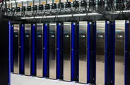 Rows of tall steel supercomputer cabinets with blue lights in a data center.