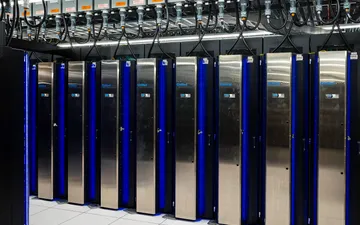 Rows of tall steel supercomputer cabinets with blue lights in a data center.